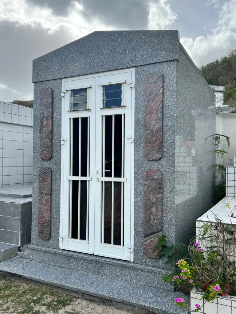 Caveau familial en granit gris avec porte vitrée et barres de protection.