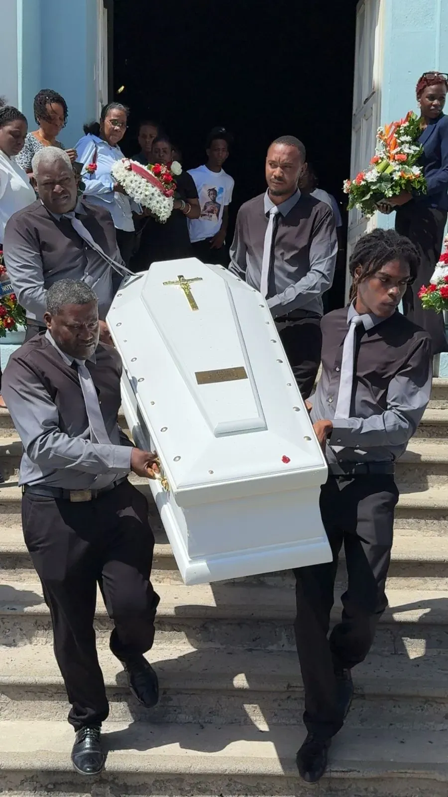 Porteurs funéraires descendant les marches avec un cercueil blanc.